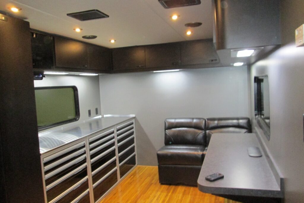 A modern interior space features a sleek kitchenette and sitting area with a leather sofa and a wooden floor.