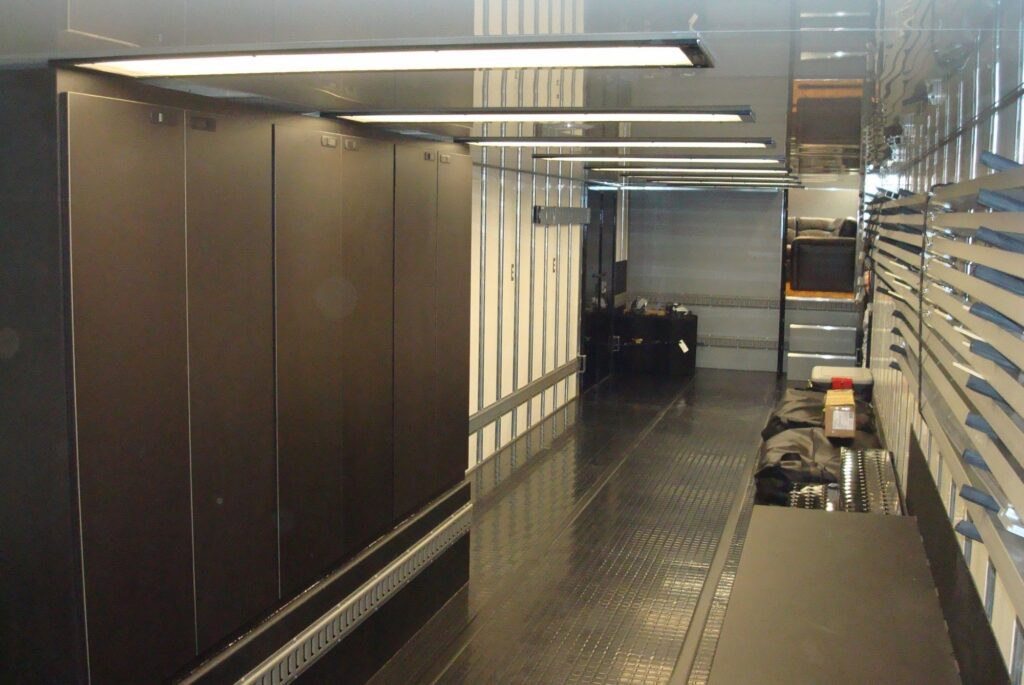 A modern kitchen interior is shown with stainless steel appliances, dark wood cabinetry, and a long countertop under bright, linear lighting.