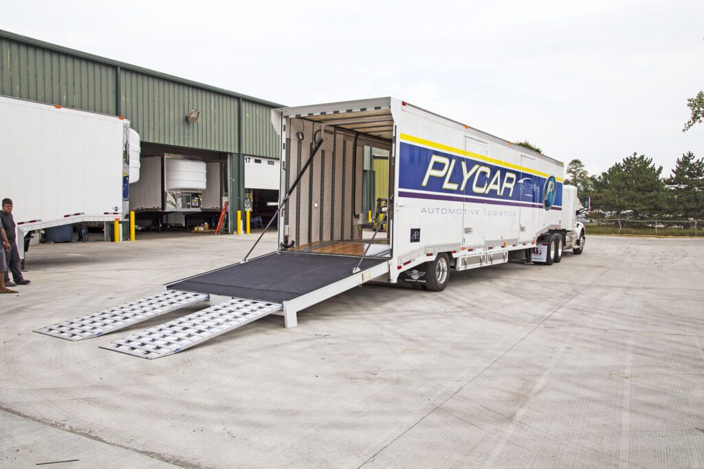 A large moving truck with an open rear door and ramp is parked outside a warehouse loading dock.