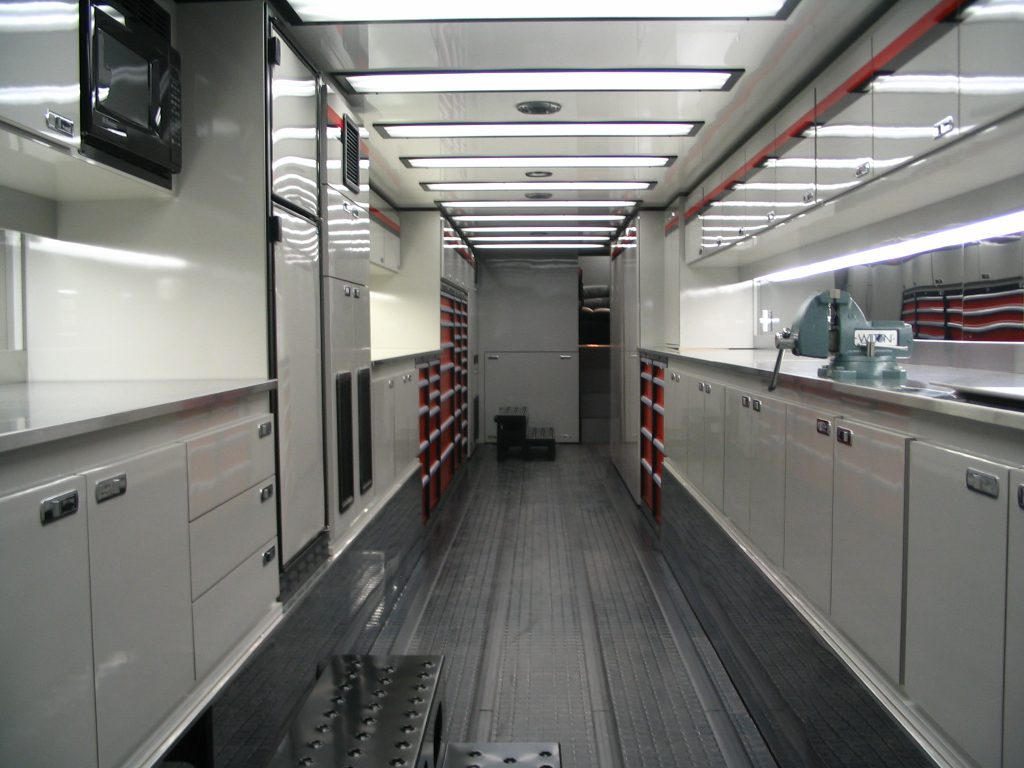 A long, narrow, and well-lit interior space with storage cabinets and shelves along the walls, and a reflective floor.