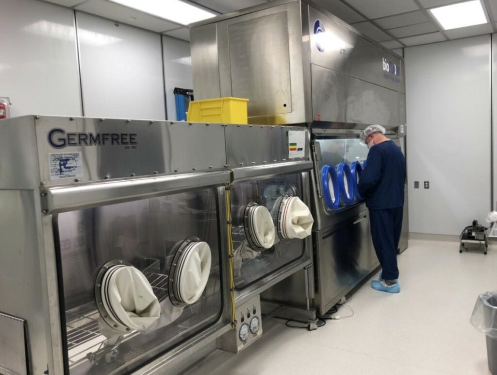 A person wearing protective clothing operates machinery in a sterile laboratory or cleanroom environment.