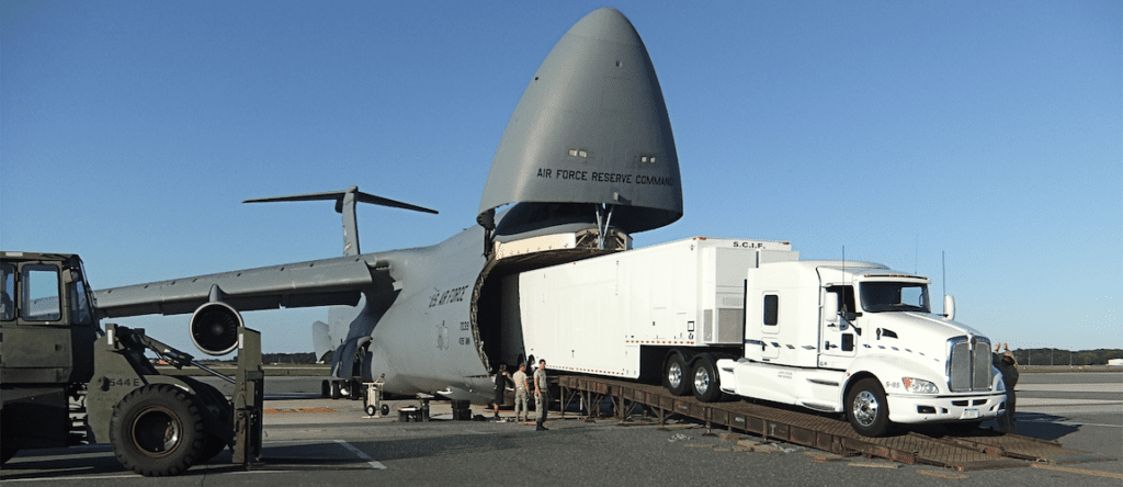 white trailer emerging from the front of a military aircraft