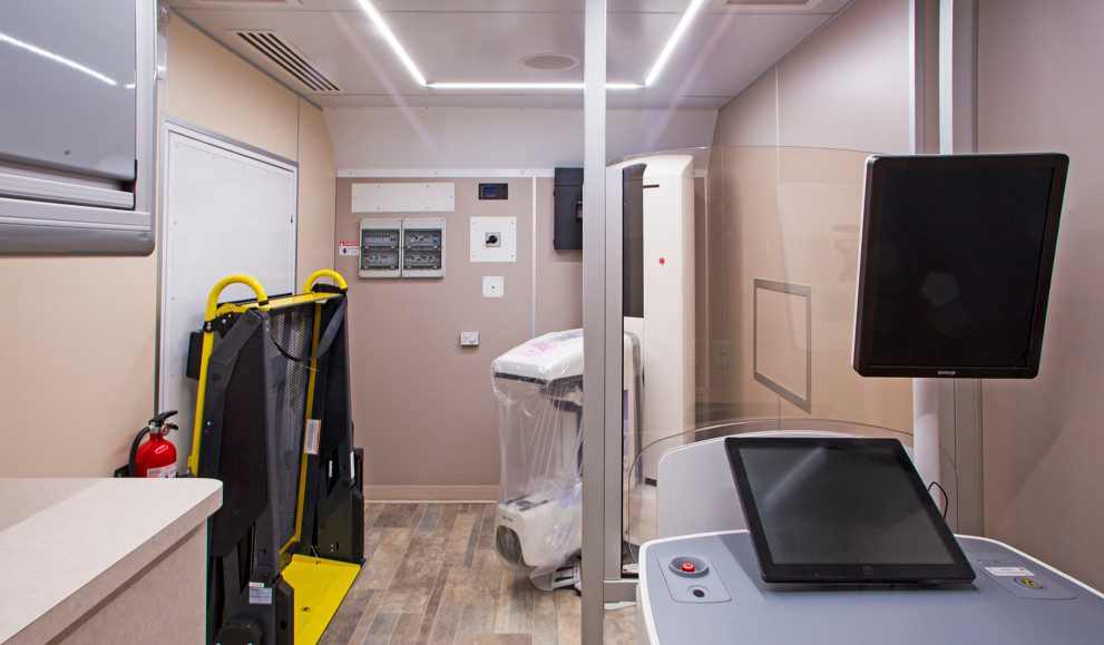 A small medical examination room features various equipment including a treadmill, diagnostic machines, and monitoring devices.